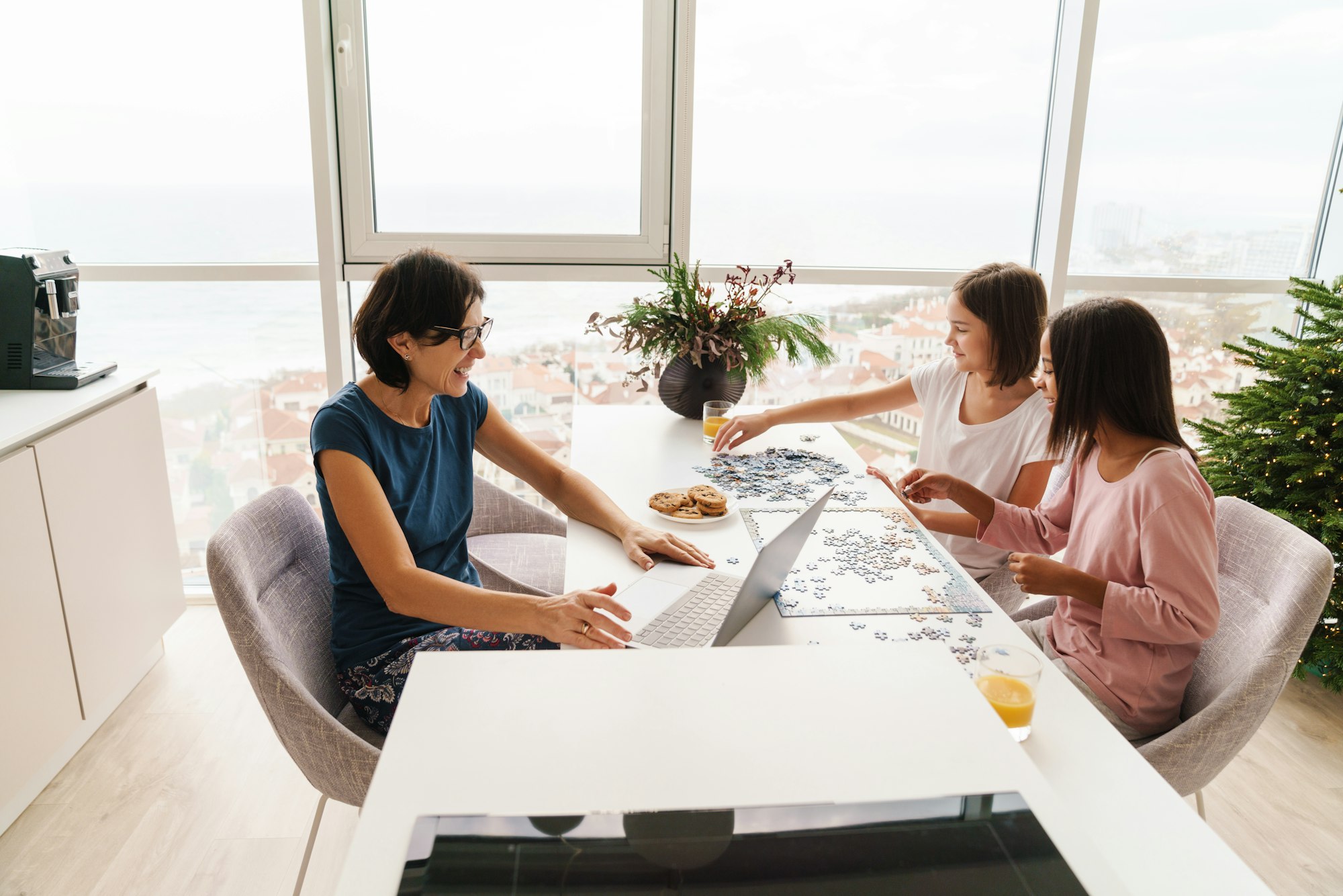 Multiracial sisters doing puzzle while their mother working with laptop