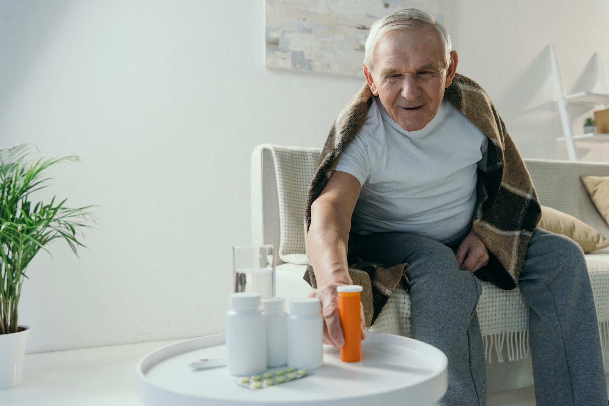 Senior sick man covered in plaid takes medications from table